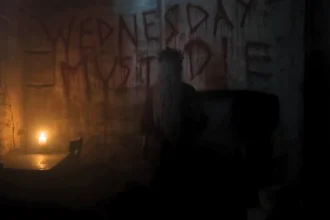 The phrase Wednesday Must Die written in blood on a dark dungeon wall, with Aunt Ophelia standing in front of it in the Wednesday Season 2 finale.