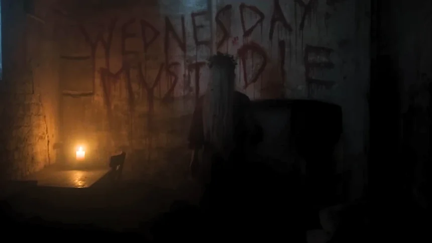 The phrase Wednesday Must Die written in blood on a dark dungeon wall, with Aunt Ophelia standing in front of it in the Wednesday Season 2 finale.